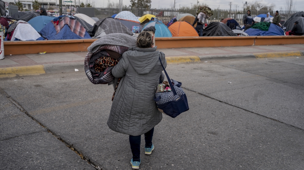 امرأة تحمل متعلقاتها إلى جزء مختلف من المخيم بالقرب من موانئ الدخول الأمريكية في حديقة تشاميزال في 19 ديسمبر 2019 في سيوداد خواريز ، المكسيك. في الوحل والبرد القارس لمخيم مؤقت في 