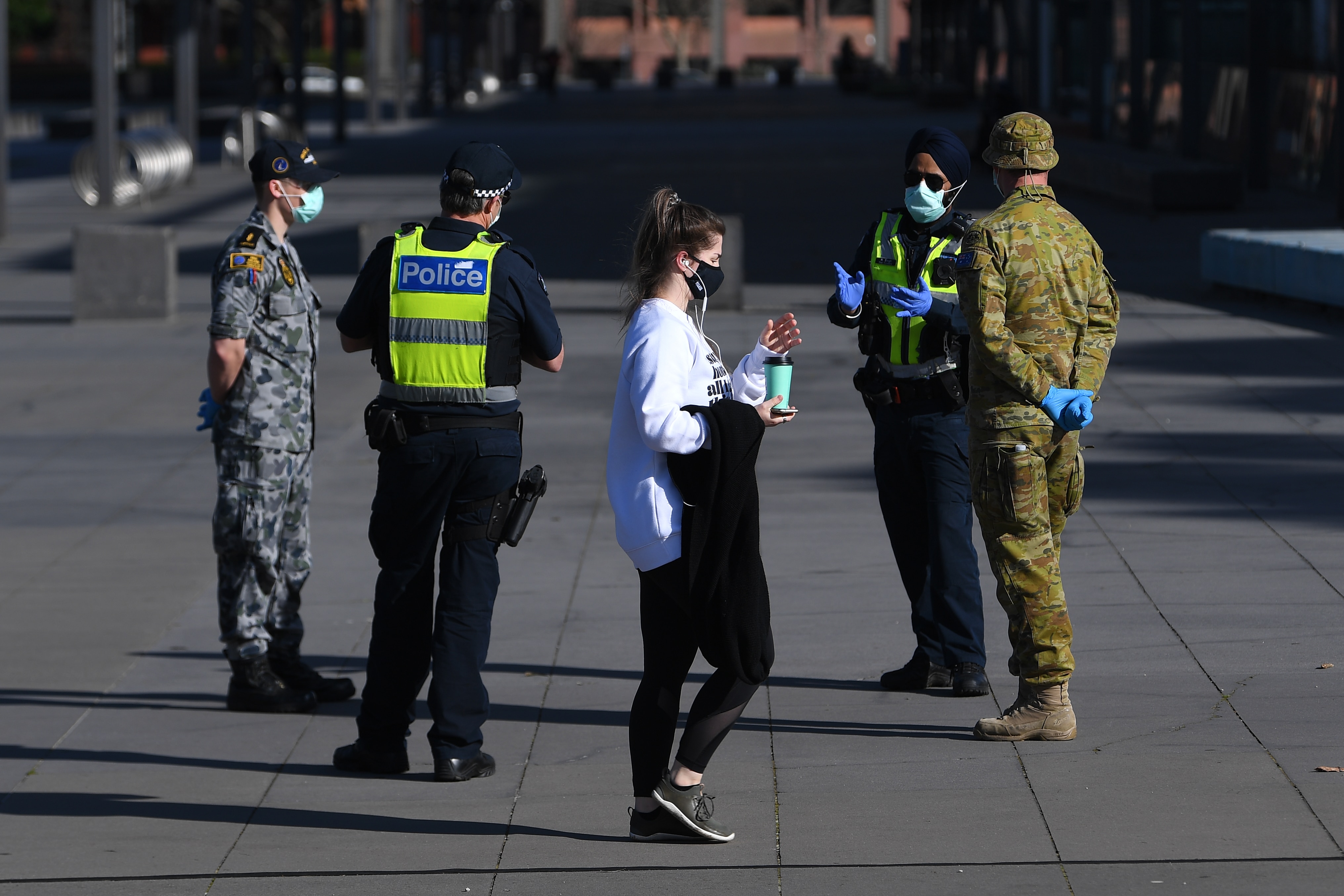 شخص يرتدي قناع وجه يمر أمام شرطة فيكتوريا والقوات الجوية وأفراد ADF خارج متحف ملبورن في ملبورن.