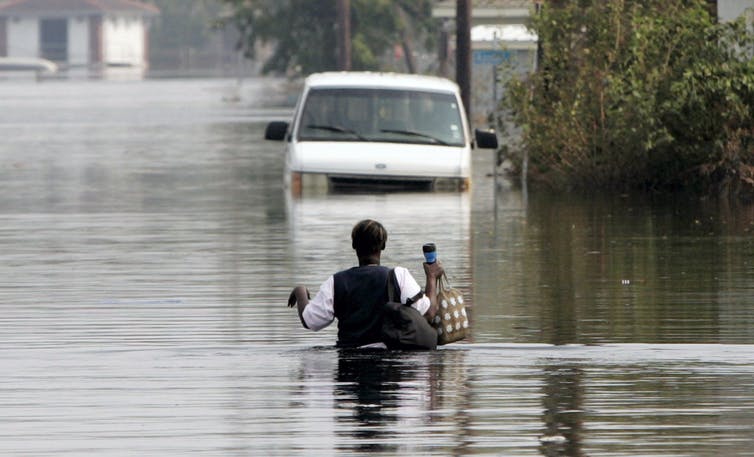 شخص يخوض في مياه فيضانات تصل إلى ارتفاع صدره باتجاه سيارة مهجورة.