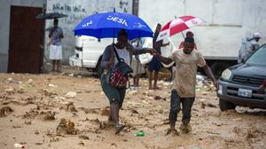 امرأة ورجل يعبران شارعًا غمرته المياه أثناء مرور العاصفة الاستوائية لورا في بورت أو برنس ، هايتي (Dieu Nalio Chery / AP)