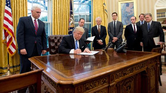 WASHINGTON, DC - JANUARY 23: (AFP OUT) U.S. President Donald Trump signs the first of three Executive Orders in the Oval Office of the White House in Washington, DC on Monday, January 23, 2017. They concerned the withdrawal of the United States from the Trans-Pacific Partnership (TPP), a US Government hiring freeze for all departments but the military, and "Mexico City" which bans federal funding of abortions overseas. Standing behind the President, from left to right: US Vice President Mike Pence; White House Chief of Staff Reince Preibus; Peter Navarro, Director of the National Trade Council; Jared Kushner, Senior Advisor to the President; Steven Miller, Senior Advisor to the President; unknown; and Steve Bannon, White House Chief Strategist. (Photo by Ron Sachs - Pool/Getty Images)